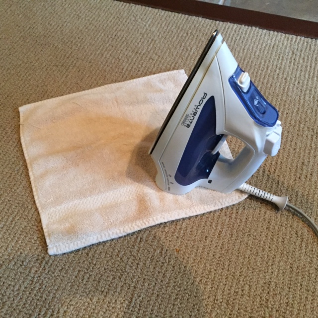 Technician using a damp cloth and iron to safely remove candle wax from a carpet