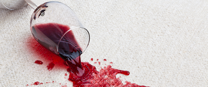 Red wine spilled on beige carpet with a cotton cloth and club soda being used to blot the stain