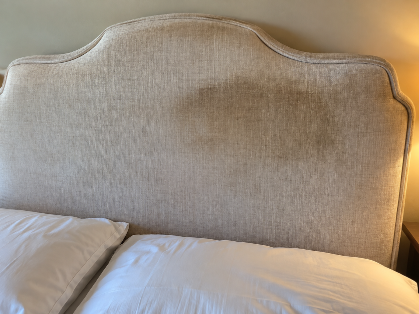 Dark oval-shaped discoloration on a light upholstered headboard from accumulated oils and everyday contact.